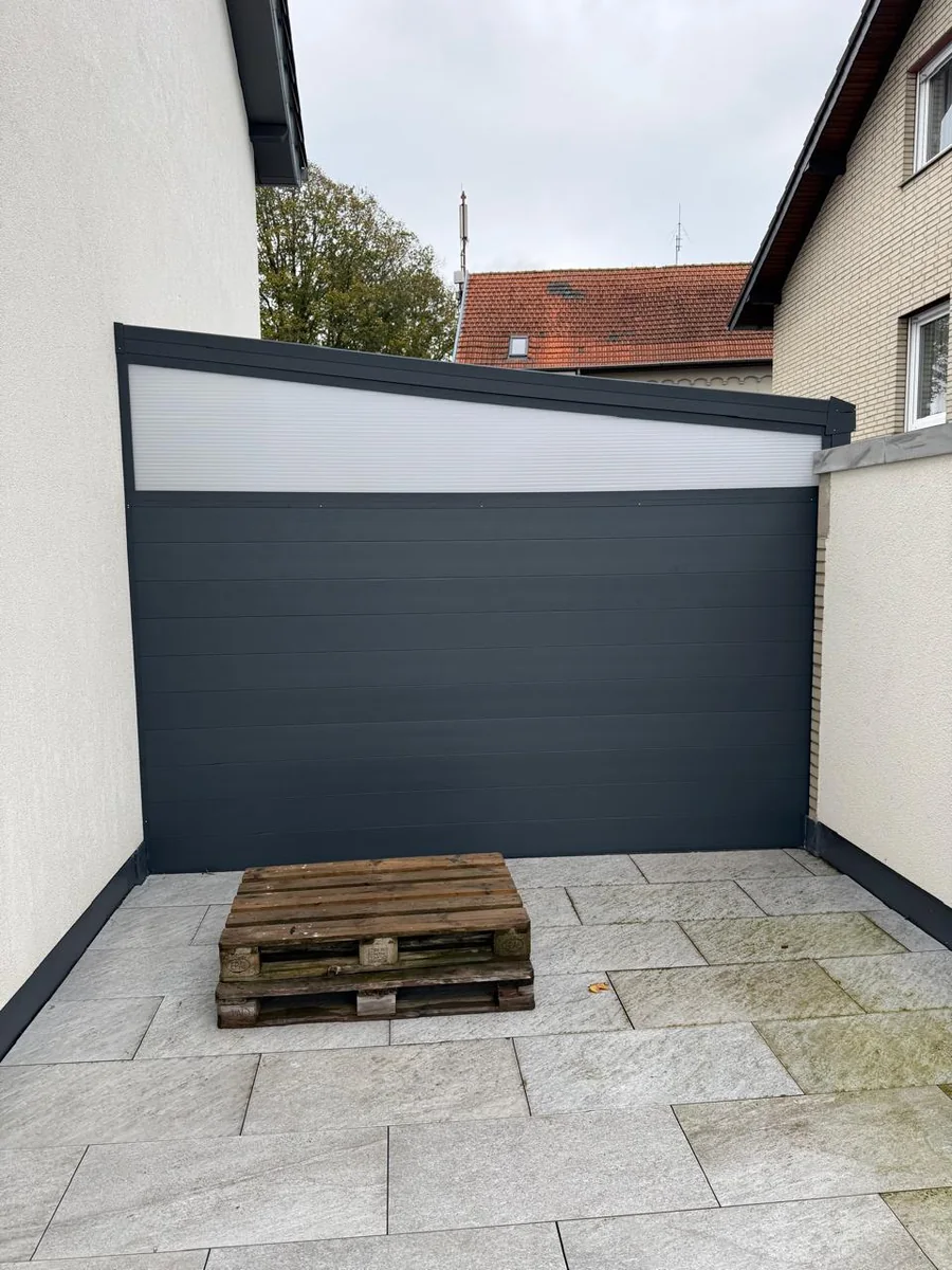 Festverglasung mit schräg zulaufender Oberkante als blickdichte Seitenwand im Innenhof