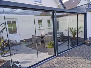 Terrassendach mit Glasschiebewand in der Eckansicht, dahinter ein Loungebereich