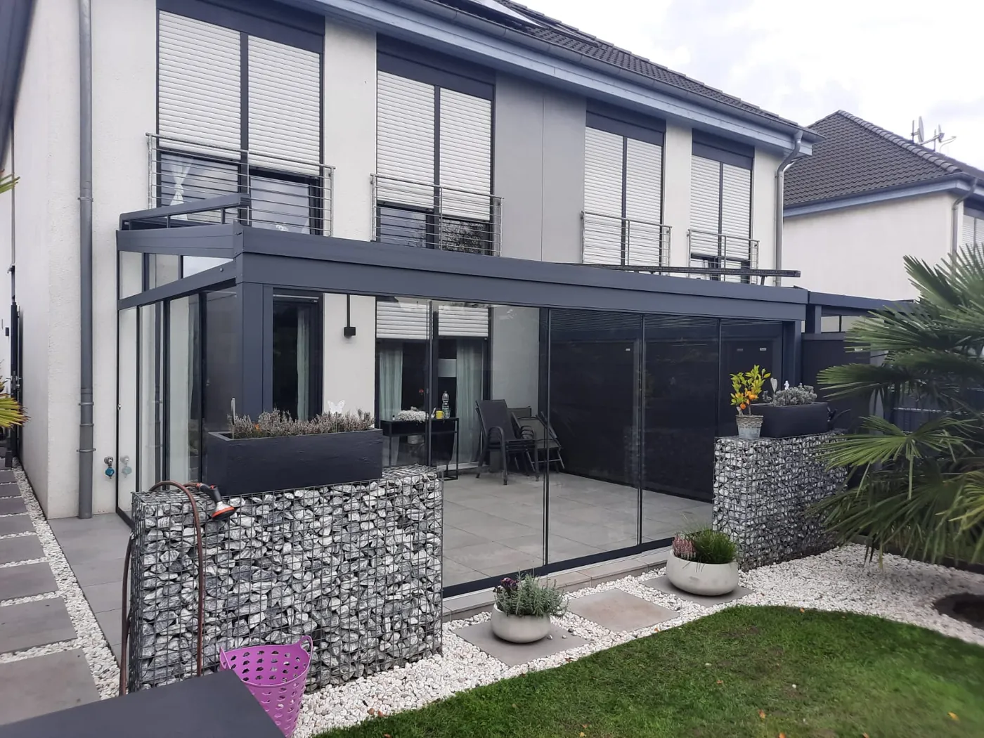 Terrassendach-Eckkonstruktion mit Glasschiebewand und Sonnenschutz unter dem Balkon